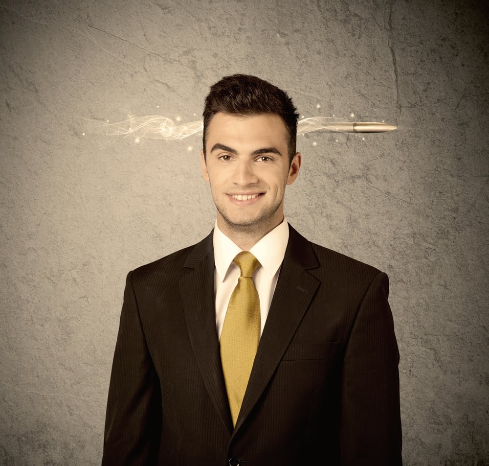 An elegant handsome business guy standing in front of wall with a bullet going through his head, making facial expressions concept